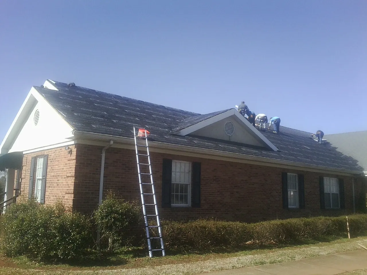 Crew tearing shingles off a brick ranch roof with a ladder set — Metal Roof Repair work by our crew in Kaneville