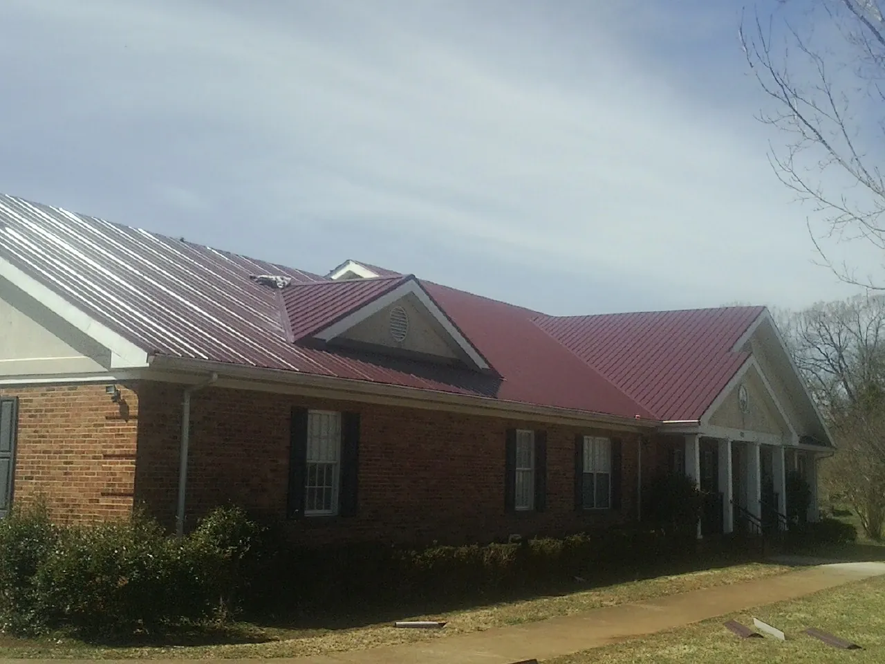 Red metal roof with gabled entries on a long brick building, from a Hail Damage Roof Repair job in Kaneville