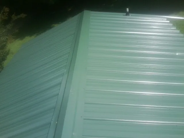 New green metal panels meeting at the ridge of a roof — Flat Roof Repair work by our crew in Kaneville