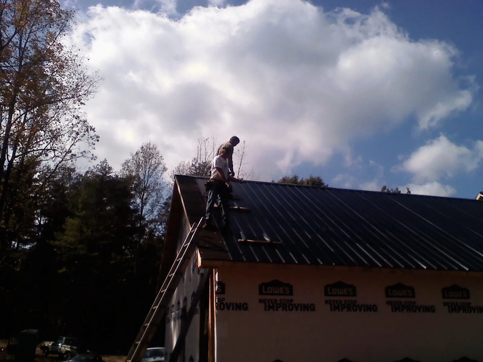 Roofer fastening dark metal panels high against a cloudy sky, from a Roof Inspection job in Kaneville