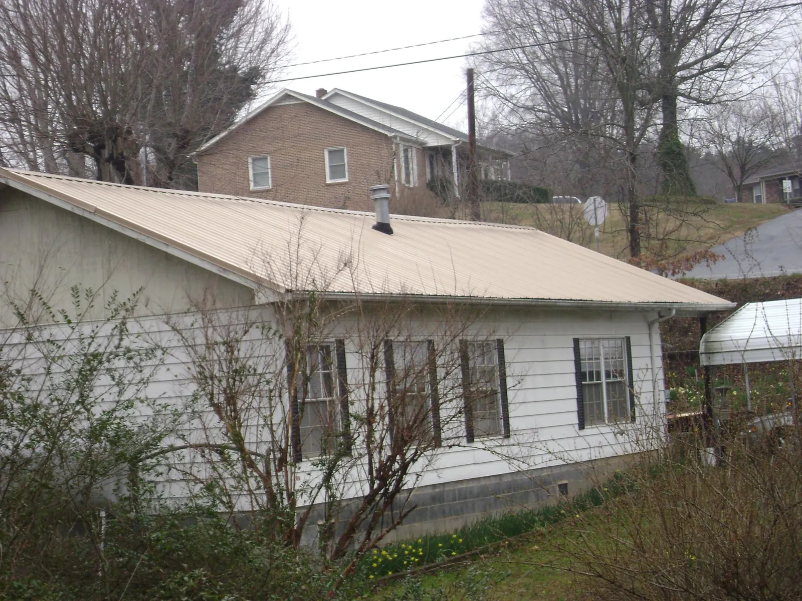 Tan metal roof on a white sided house set into a hillside — Commercial Roofing by Roofing Brothers in Kaneville